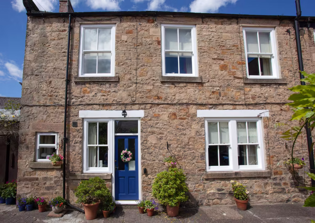 The rear of The Back House Staindrop, a holiday home in County Durham, made up of sandstone with a blue door and foilage